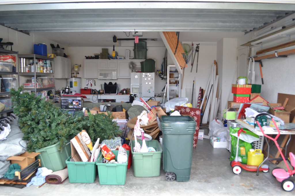 A cluttered garage full of stuff from Christmas decorations to bins and garbage cans. 