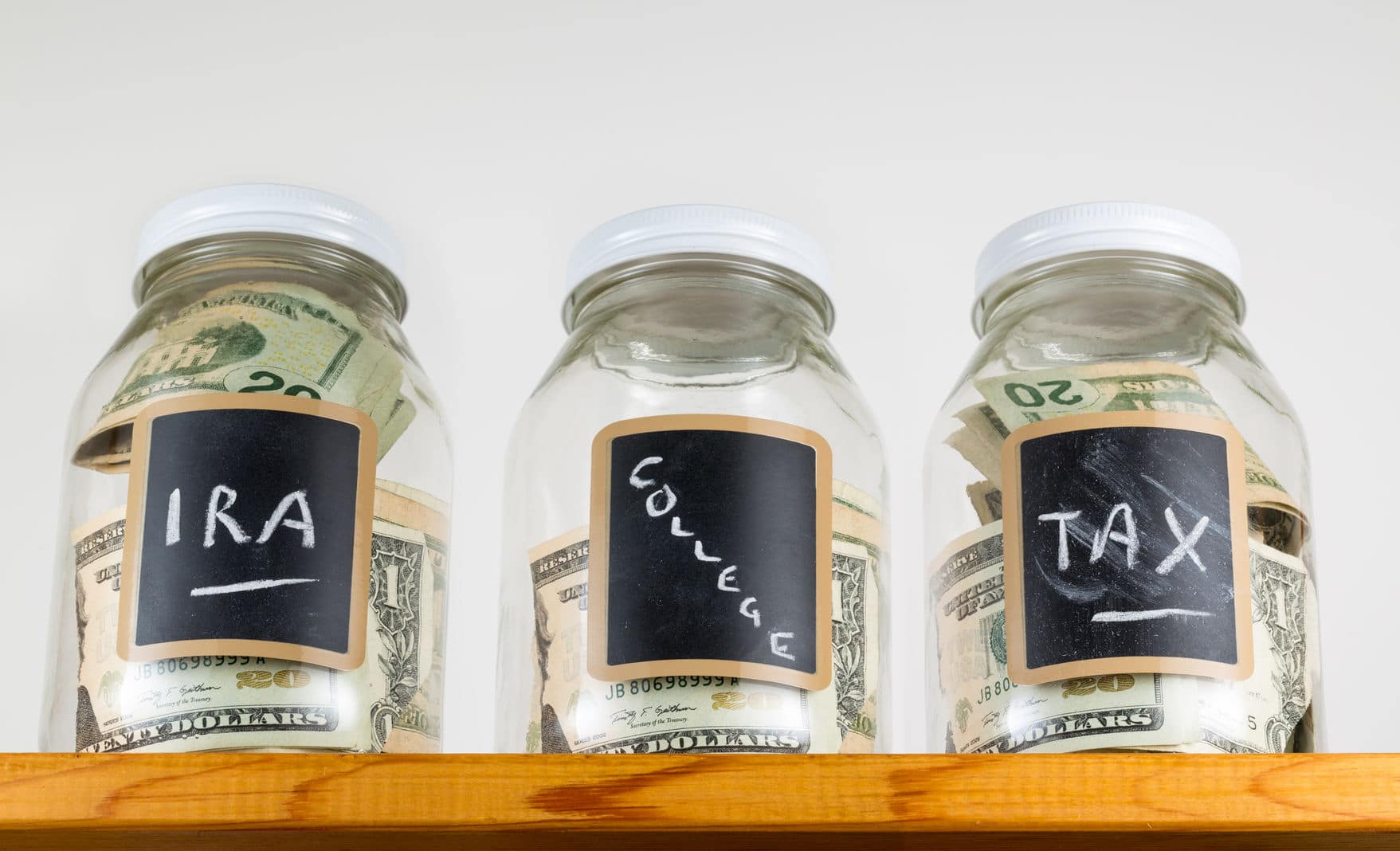 Different mason jars with cash labeled, IRA, College and Tax. 