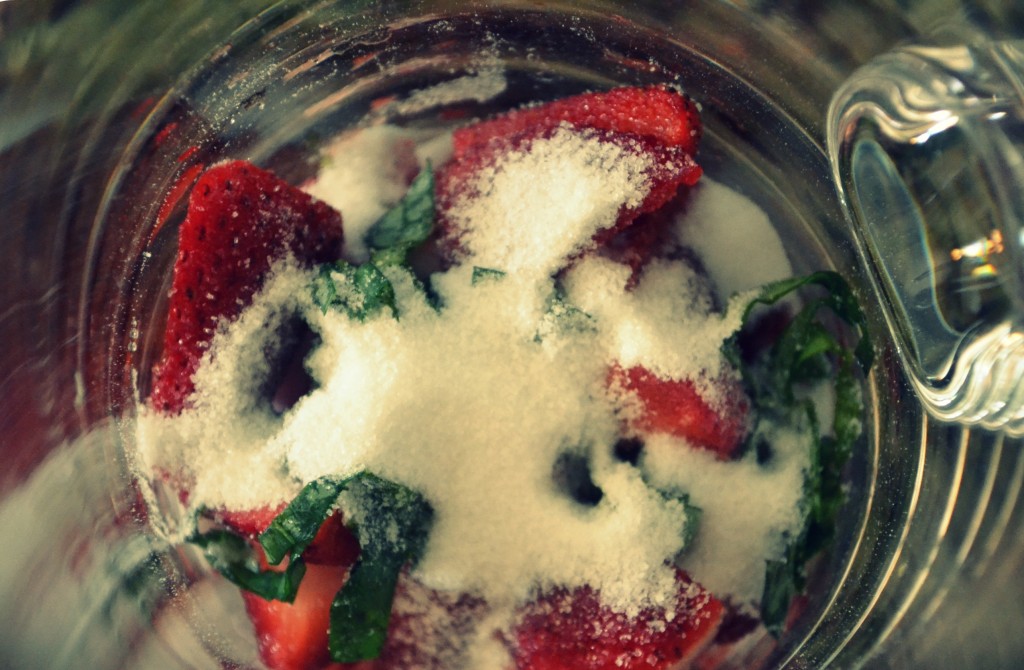 Slice strawberries and basil and put them into the bottom of a large pitcher, then add sugar. 
