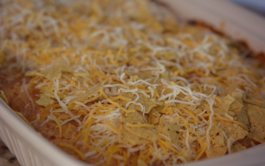 Sprinkle tortilla chips and shredded cheese on top of taco casserole 