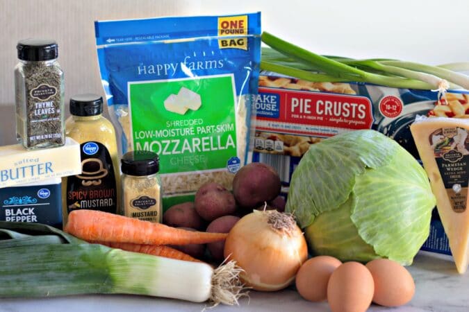 Assemble your ingredients, butter, eggs, potatoes, onions, carrots, green onion, cheese, pie crust, salt, pepper, mustard and cabbage 