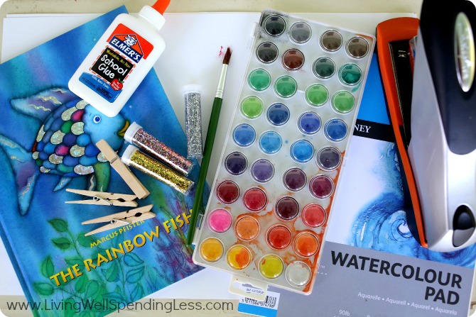 Assemble your materials to make your rainbow fish puppets: Card stock or watercolor paper, watercolor paints and brush, glue, glitter, scissors, clothes pins and the Rainbow Fish book. 