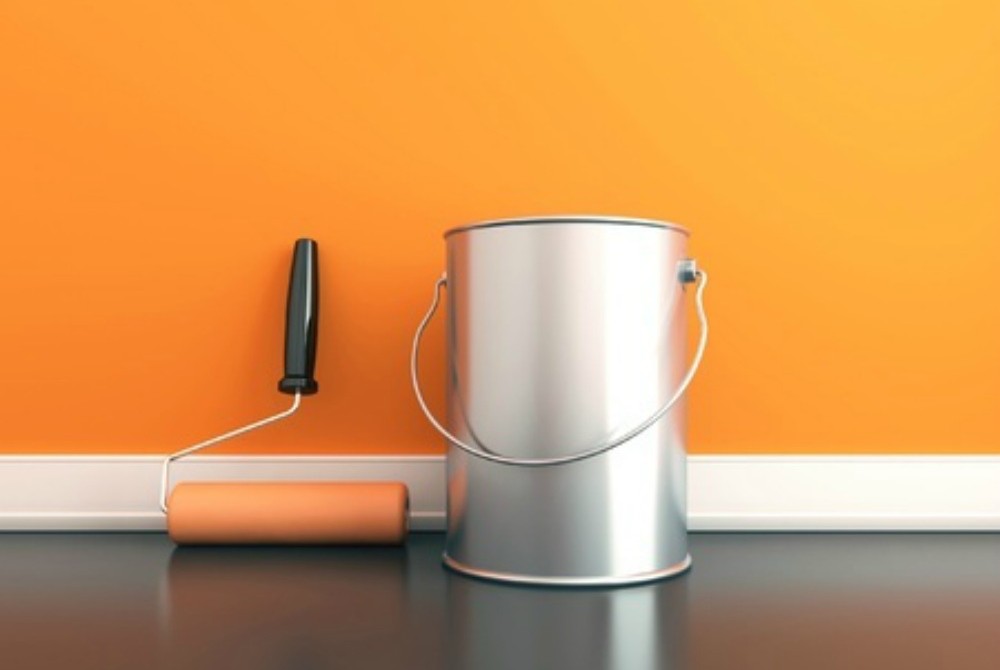 A paint can and roller paint brush resting against an orange wall. 