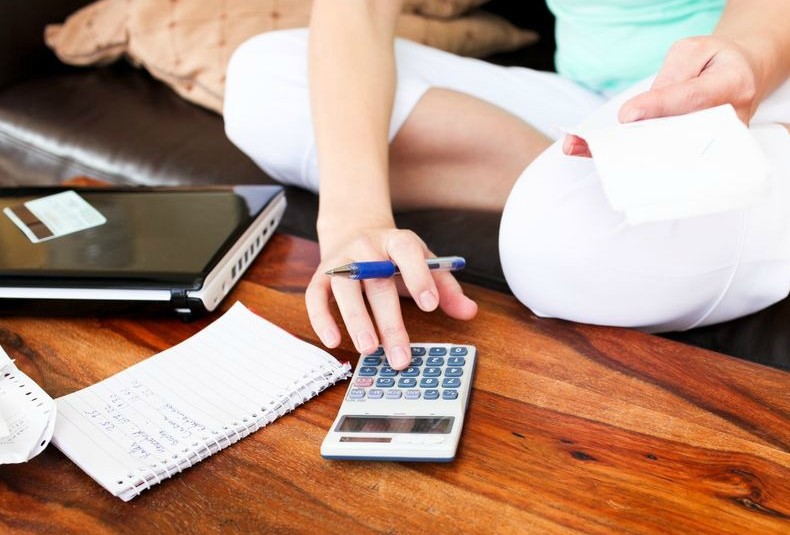 A woman tracking her expenses with a calculator and small notebook. 