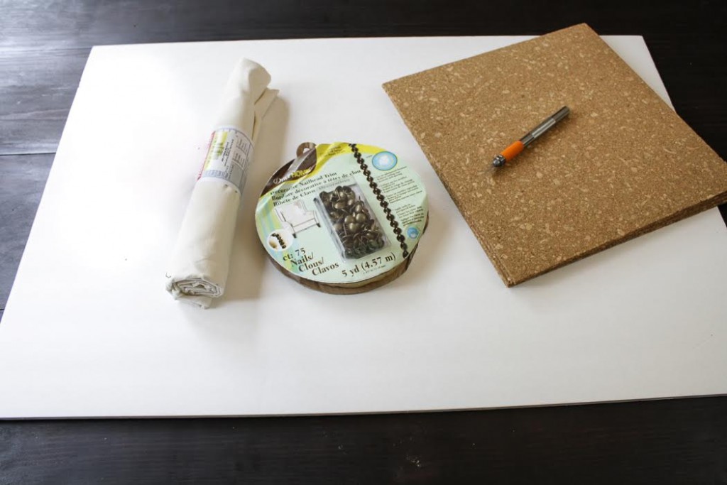 Assemble the materials you need: A piece of fabric, foam core board, cork tiles, nailhead trim , Mod Podge, an office stapler, scissors and a craft knife.