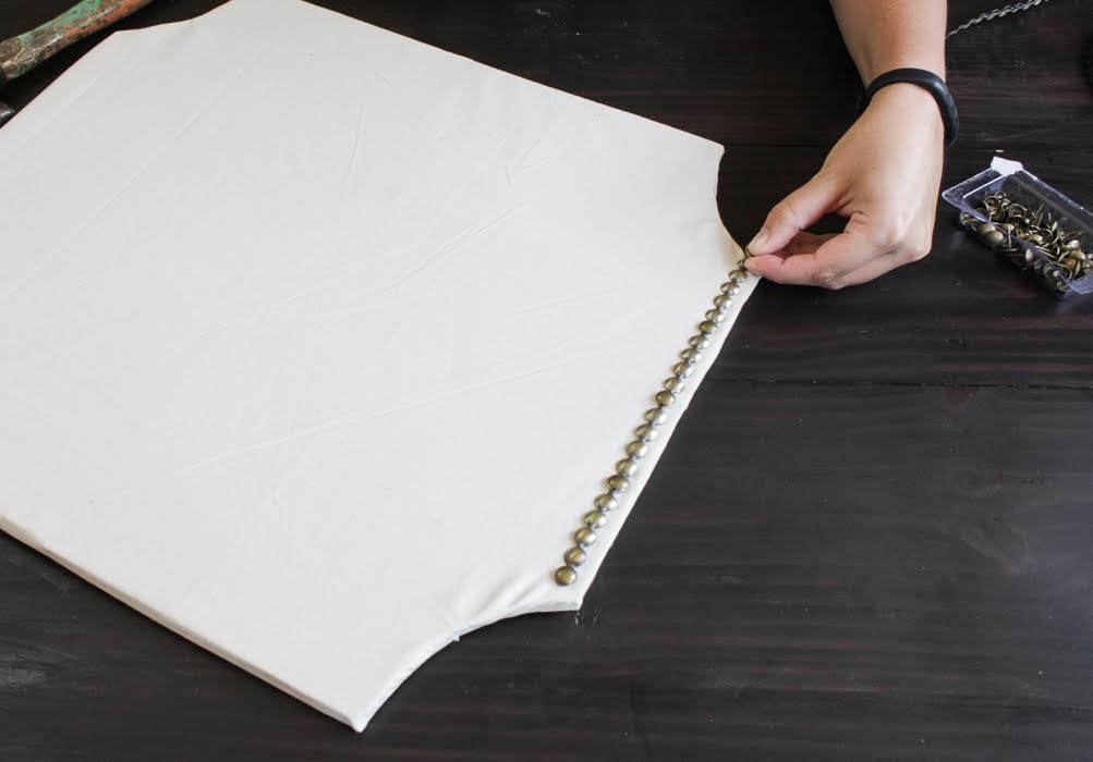 Use nail heads to secure the fabric piece to the cork board. 