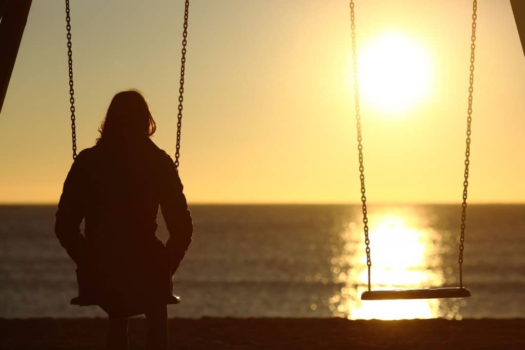 It's lonely when friends let you down: a woman alone on a swing overlooking the water. 