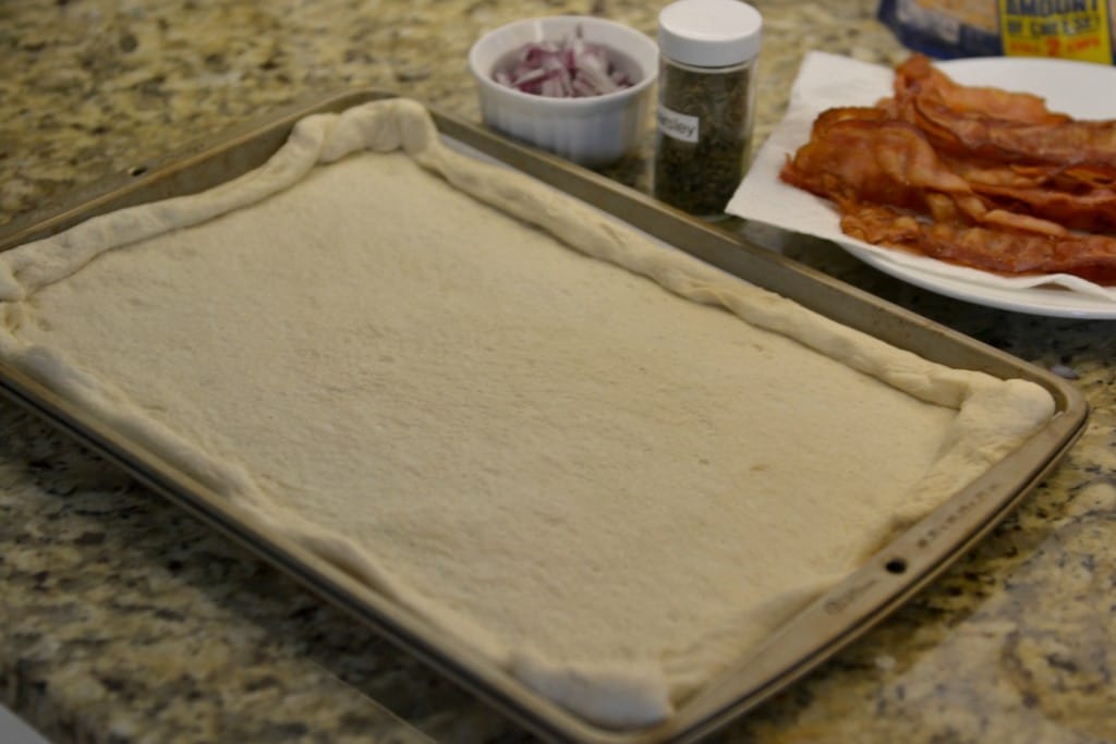 Unroll pizza crust onto parchment paper covered cookie sheet.