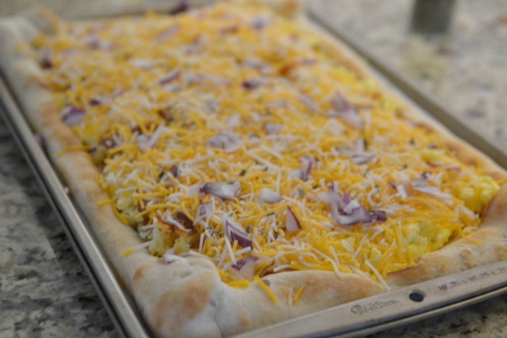 Add cheddar cheese then red onion over bacon and egg mixture on pizza crust. 