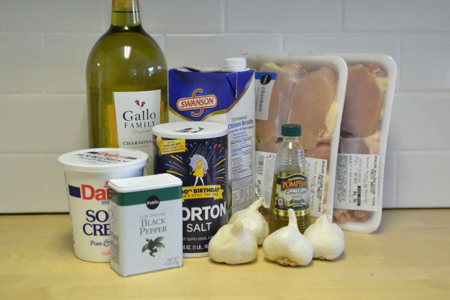 Assemble your ingredients for the garlic chicken including: Olive oil, white wine, chicken broth, sour cream, salt, pepper, boneless skinless chicken thighs, garlic, and fresh thyme. 