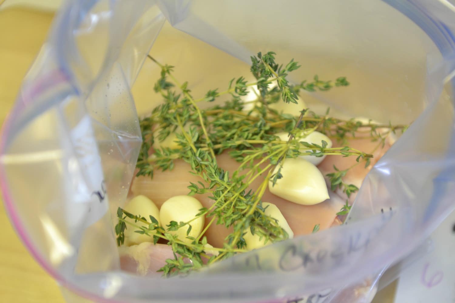 Divide chicken into 1-gallon freezer bags then divide garlic cloves and thyme into bags over top of chicken. 