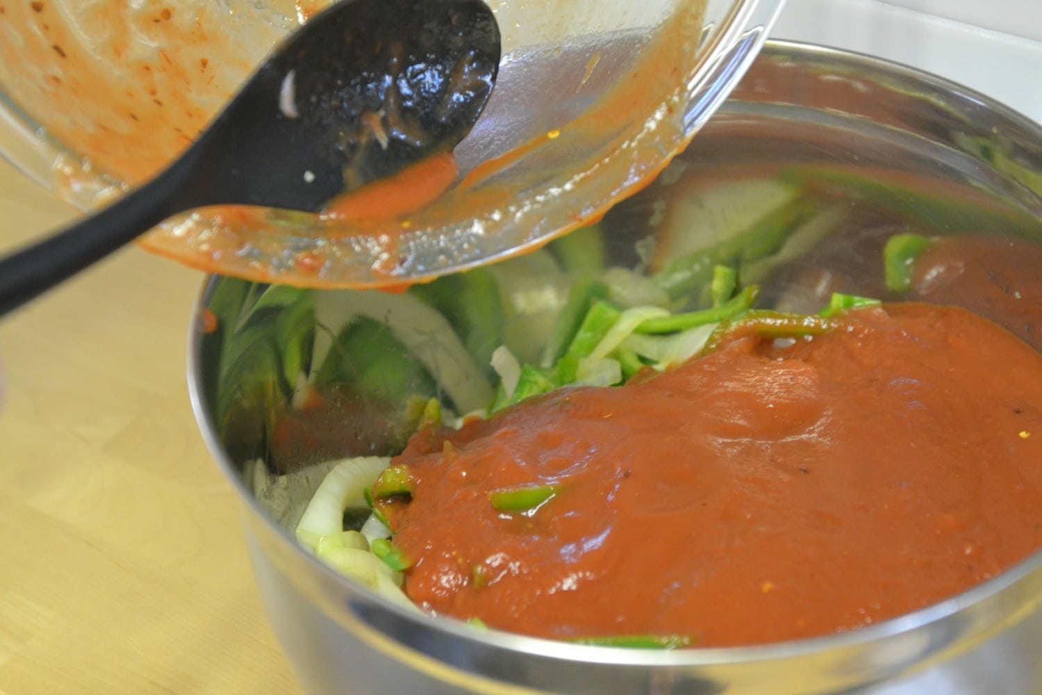 Spoon the tomato sauce with spices over the top of the peppers and onions in a mixing bowl. 