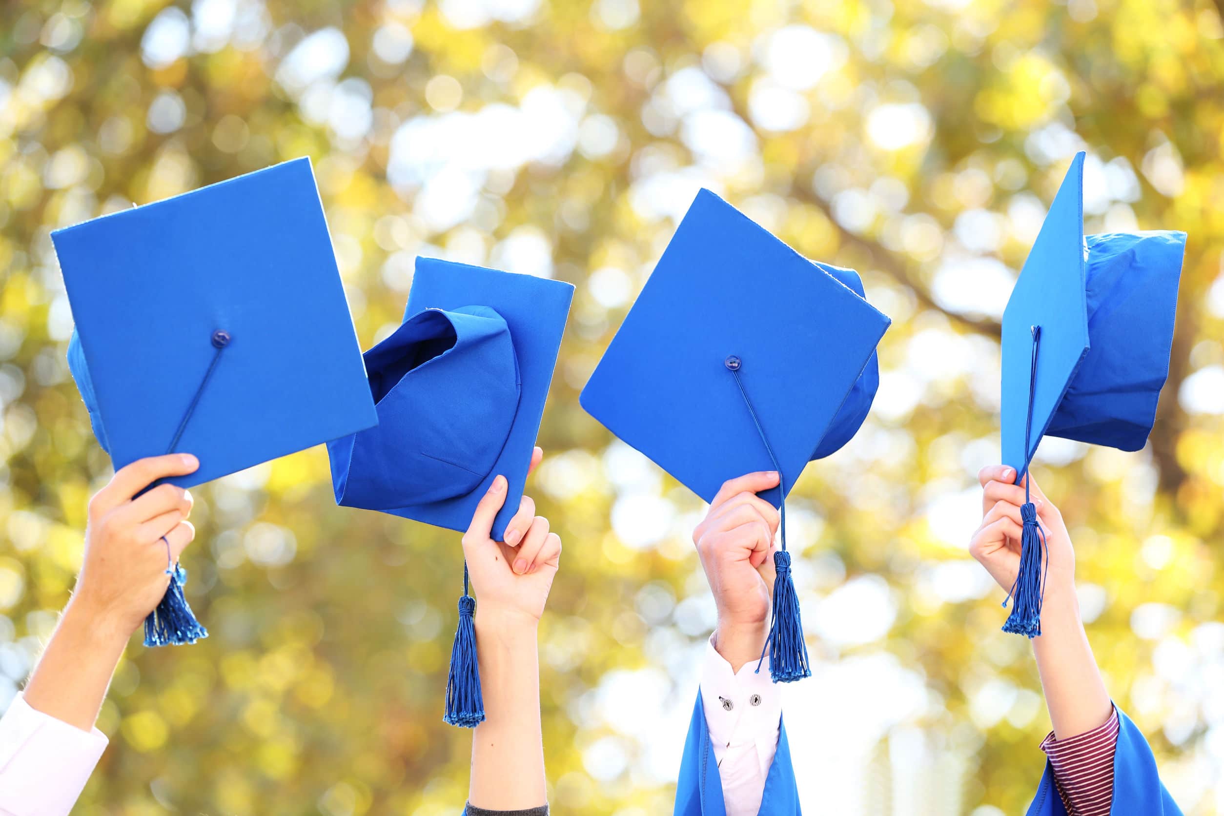 Graduates holding up their caps and tassels on a sunny day. 