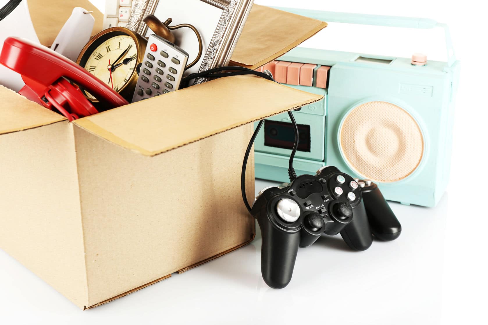 A box of various items including a clock, remote, video game controller and radio. Step one de-clutter.