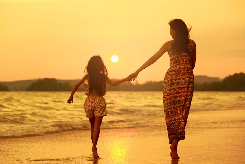 A mother and daughter running on the beach as the sun sets. 