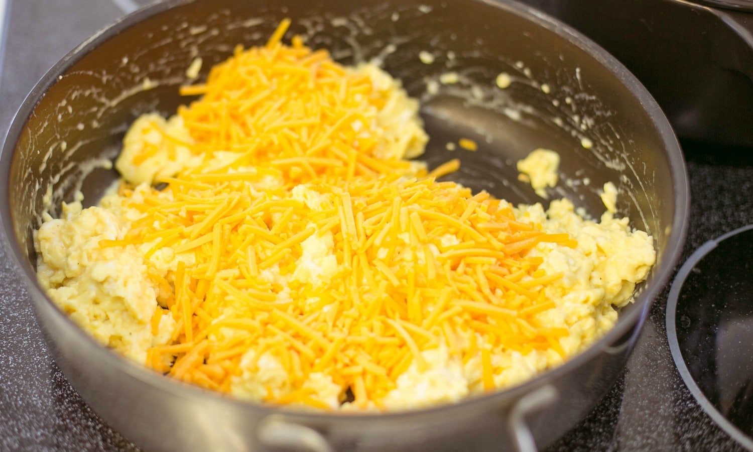 Add shredded cheddar cheese to the scrambled eggs