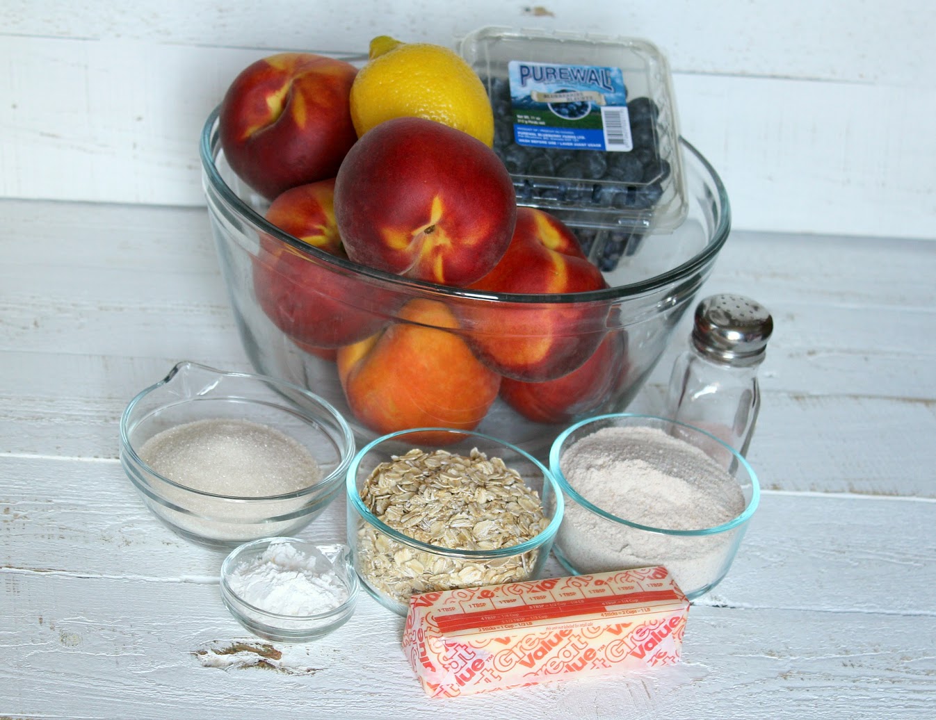 Assemble the ingredients for this yummy summer crumble: peaches, oats, sugar, butter, blueberries and a lemon.