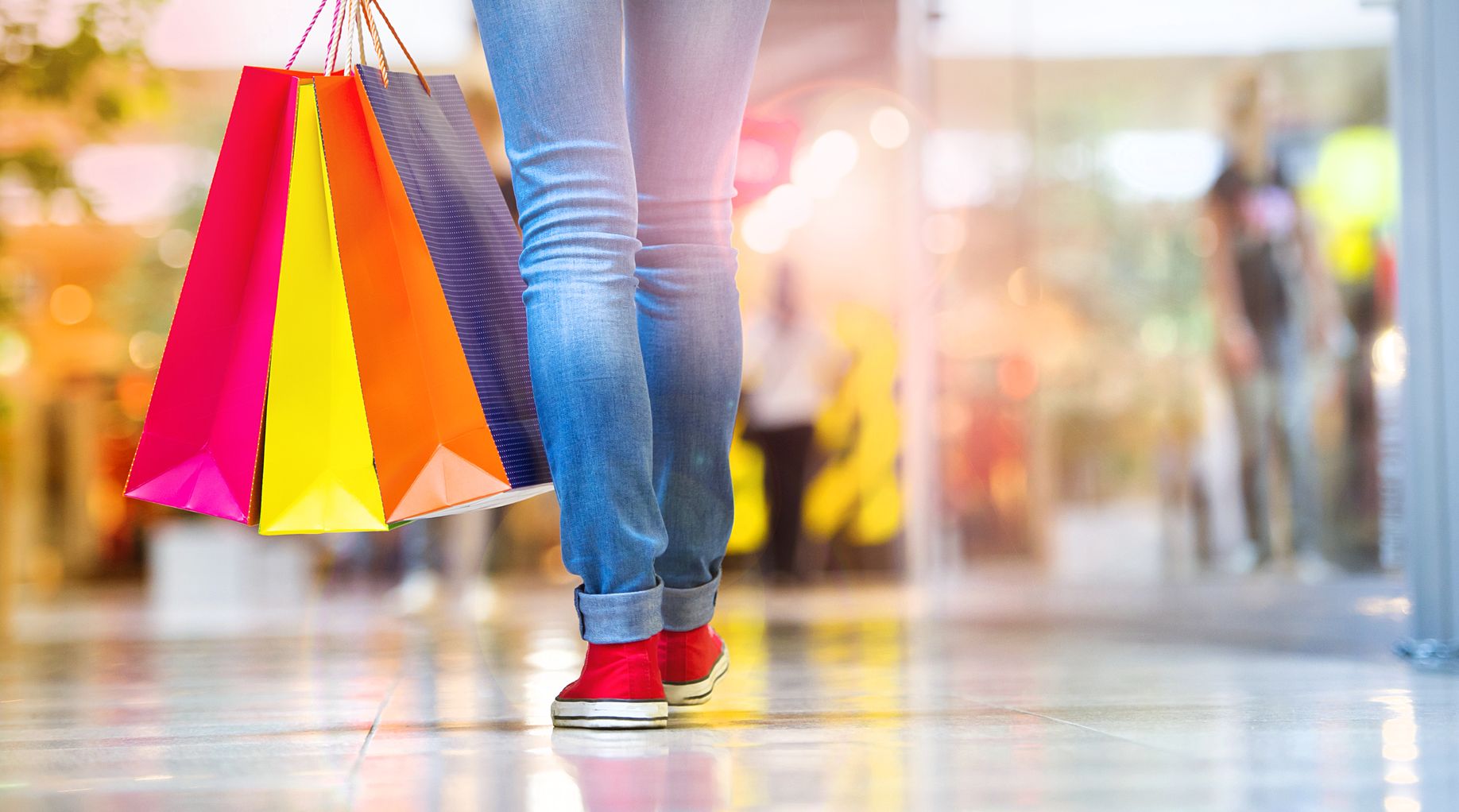 A woman's feet walking through a mall holding shopping bags. 