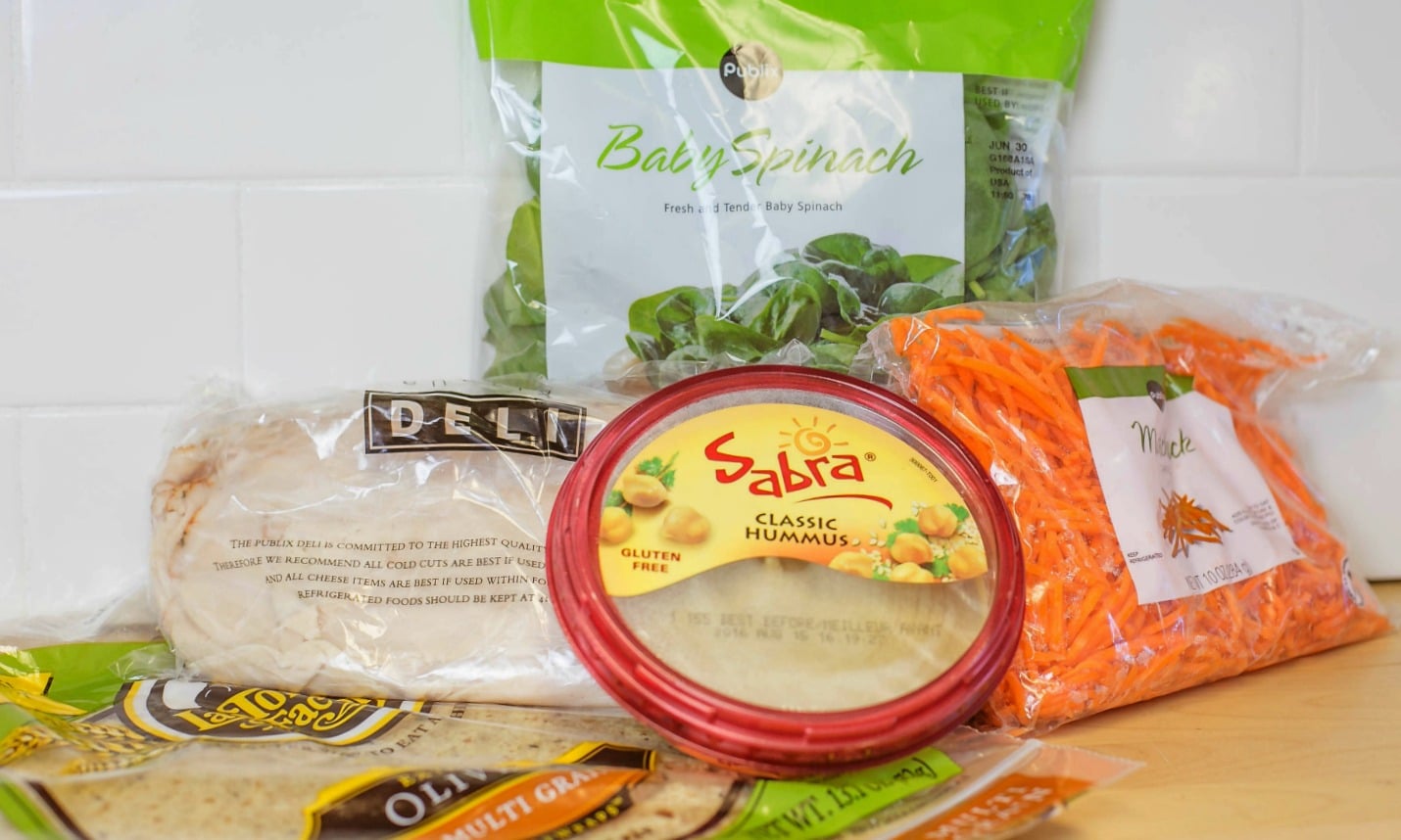 Assemble the ingredients for these quick and easy, make-ahead wraps: deli meat, hummus, spinach, carrots and wraps.