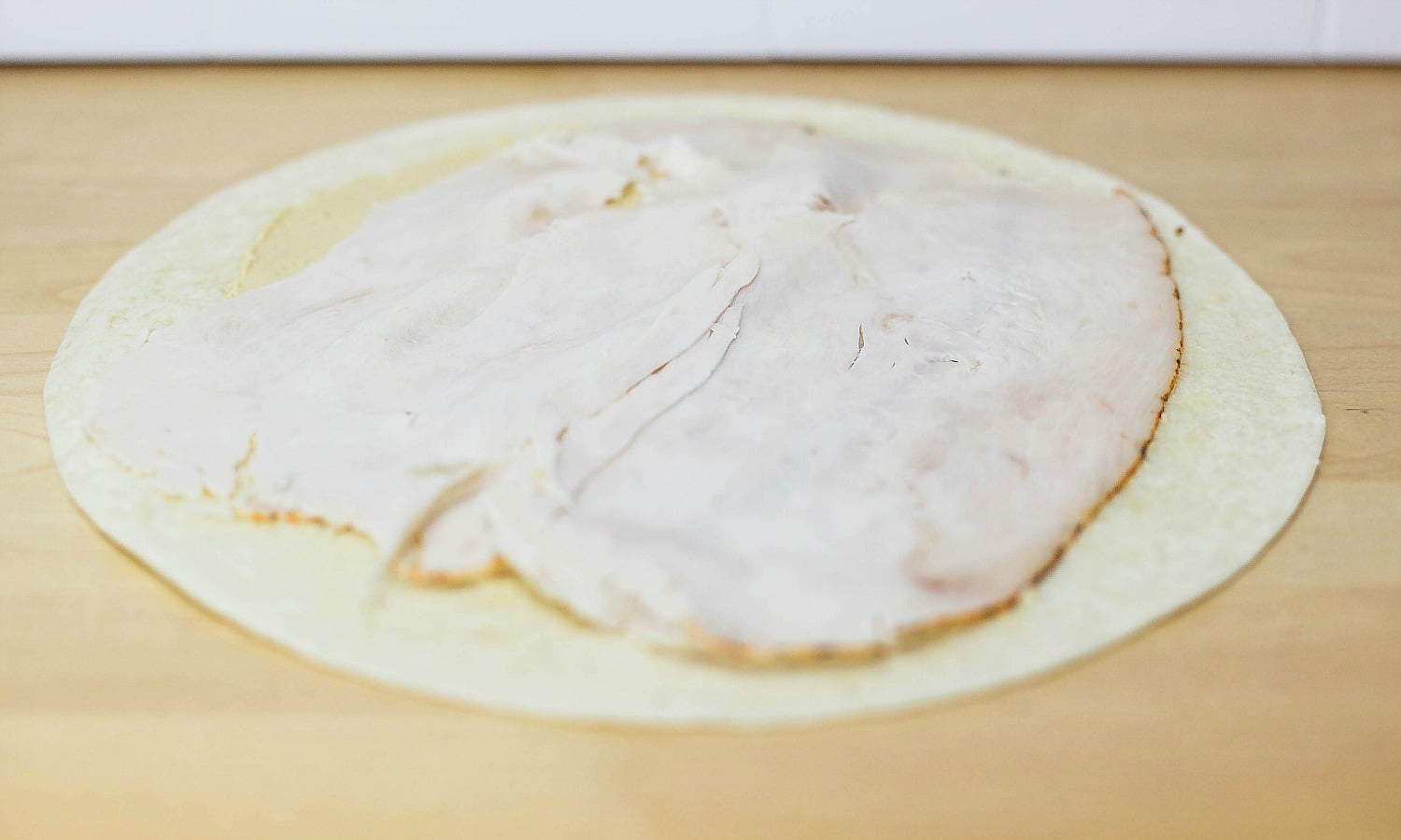 Layer thin slices of turkey on top of the hummus for your make-ahead wrap. 