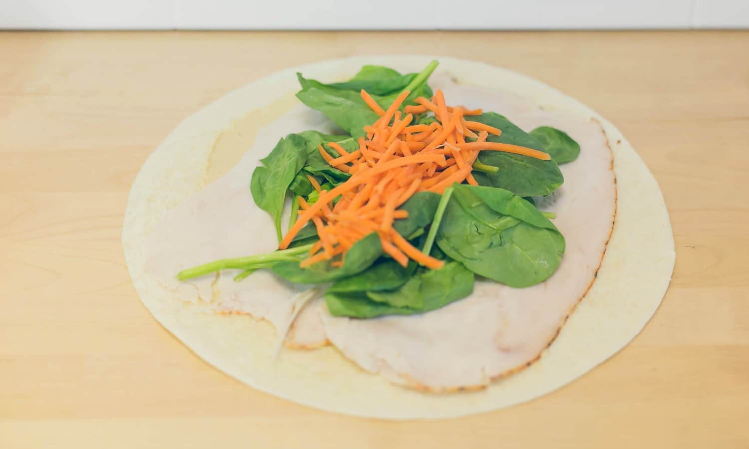 Add a layer of spinach and carrots to the middle of the wrap.