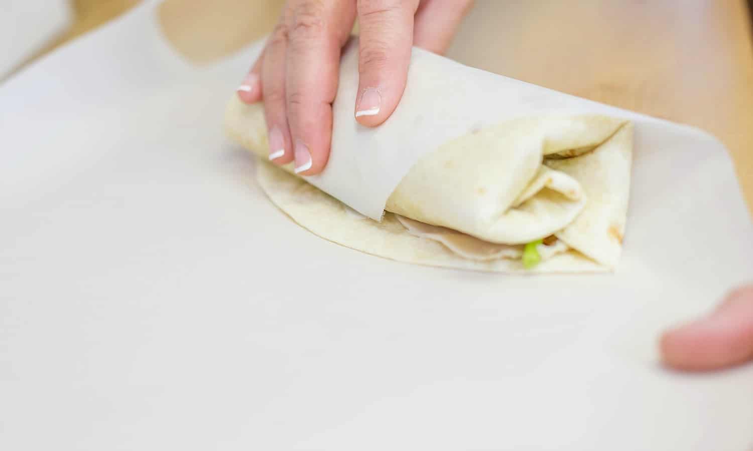 Roll the wrap, using parchment paper to get a tight roll, while folding in the ends like a burrito.