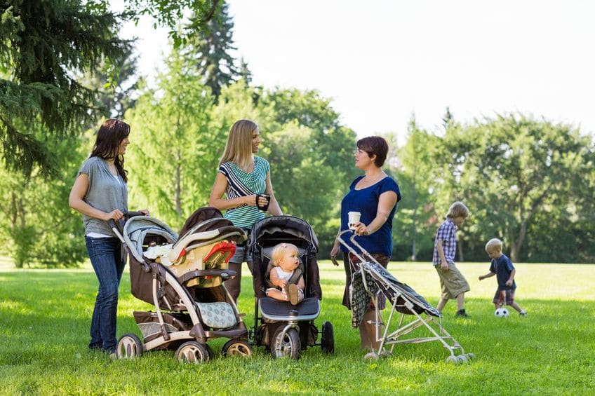 A group of mothers standing outside with their children in strollers. 