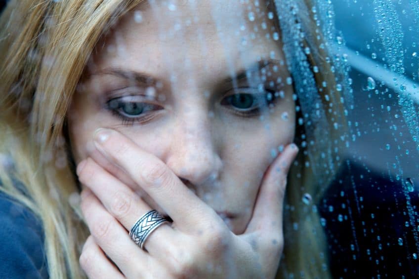 A woman who is sad gazing out of a window as it rains. 