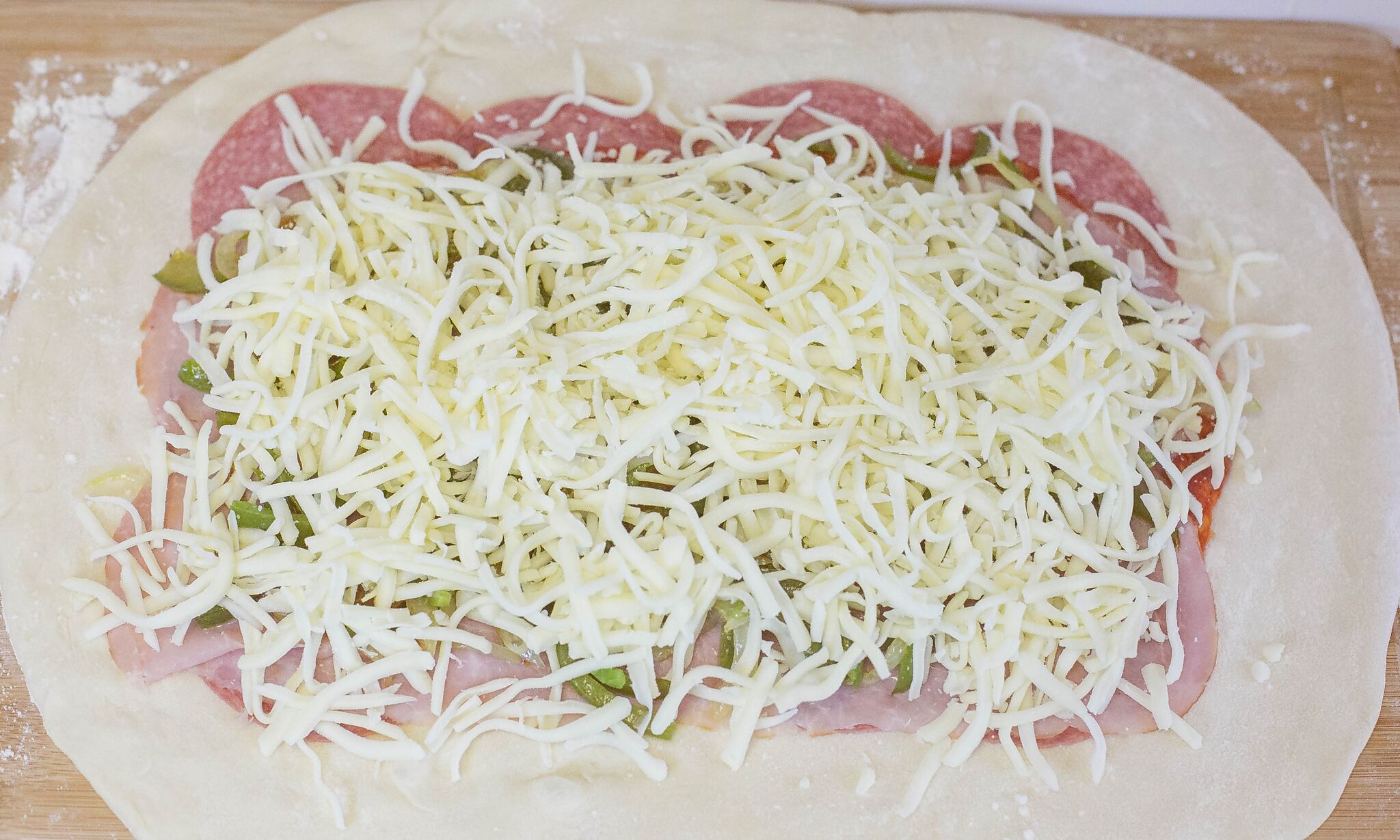 Layer salami, pepperoni, ham, onions, peppers, and cheese onto the dough. 
