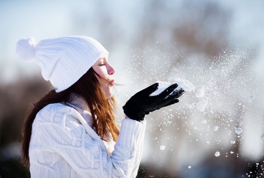 Woman enjoys the winter while blowing snow into the air. 