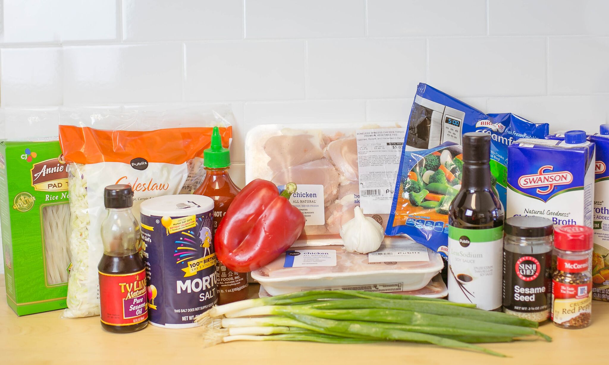 Assemble your ingredients: Chicken thighs, frozen vegetables, soy sauce, garlic, green onions, red bell pepper, chicken stock, rice noodles, shredded slaw mix, sesame seeds, spicy sauce, sesame oil, red pepper flakes and sriracha sauce. 