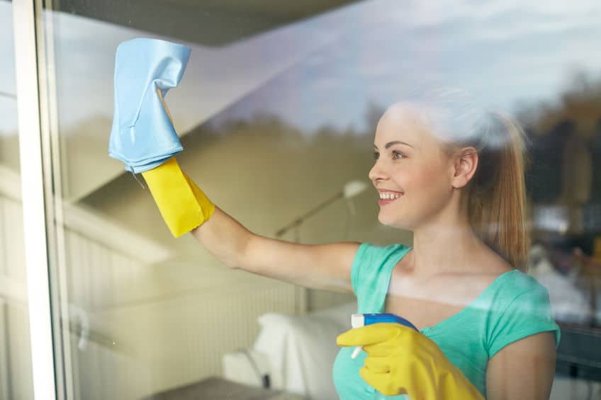 A woman cleaning windows with spray, rubber gloves and a rag. 