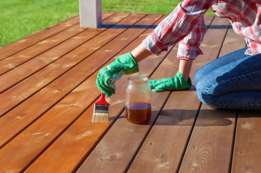 Using rubber gloves, a mason jar and a paint brush, apply protective sealant to the wooden deck. 