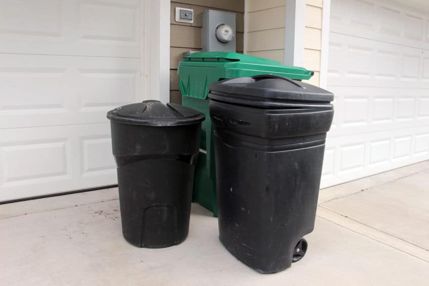 Several garbage bins outside of a garage. 
