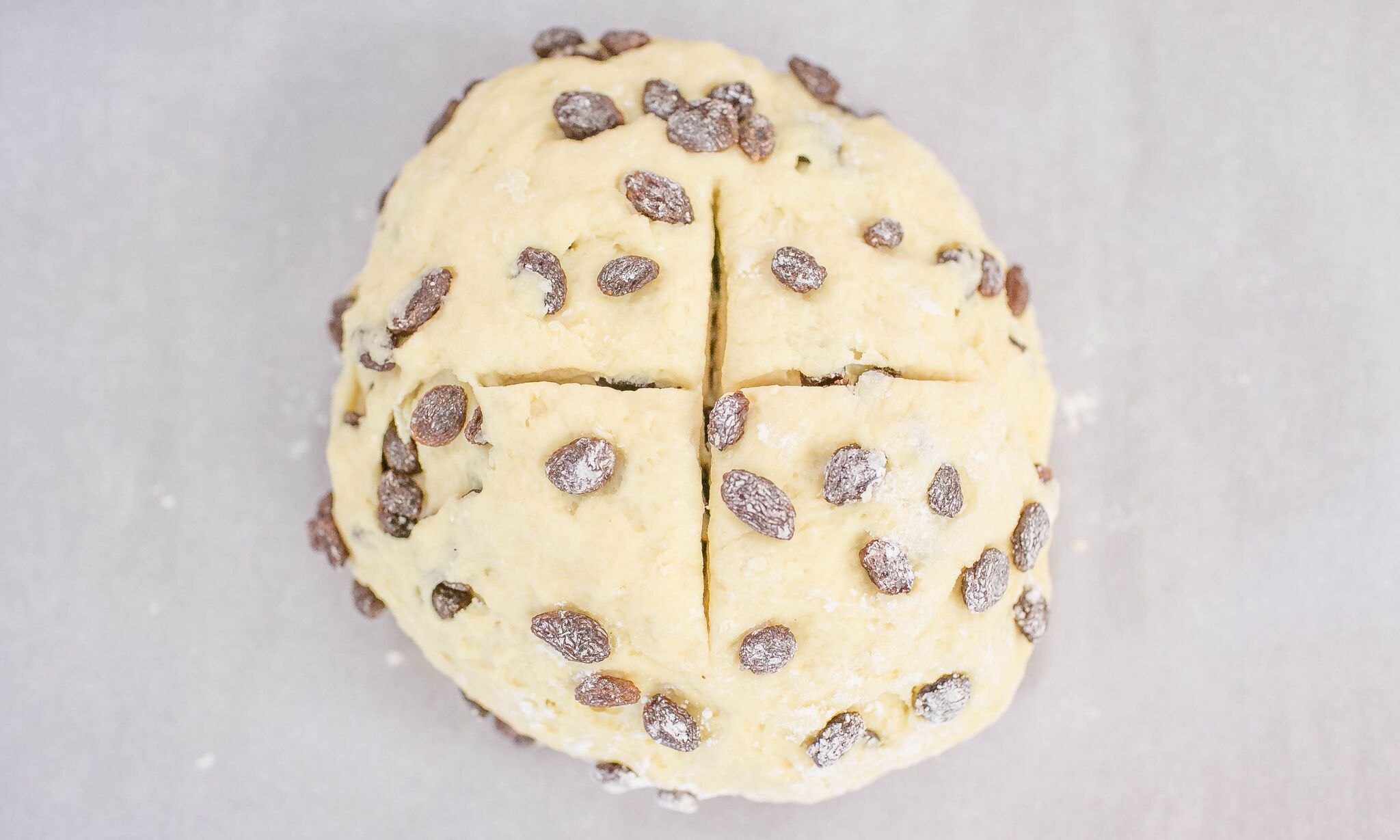 Roll the dough into a ball on a floured surface. Then split the dough with a cross on top. 