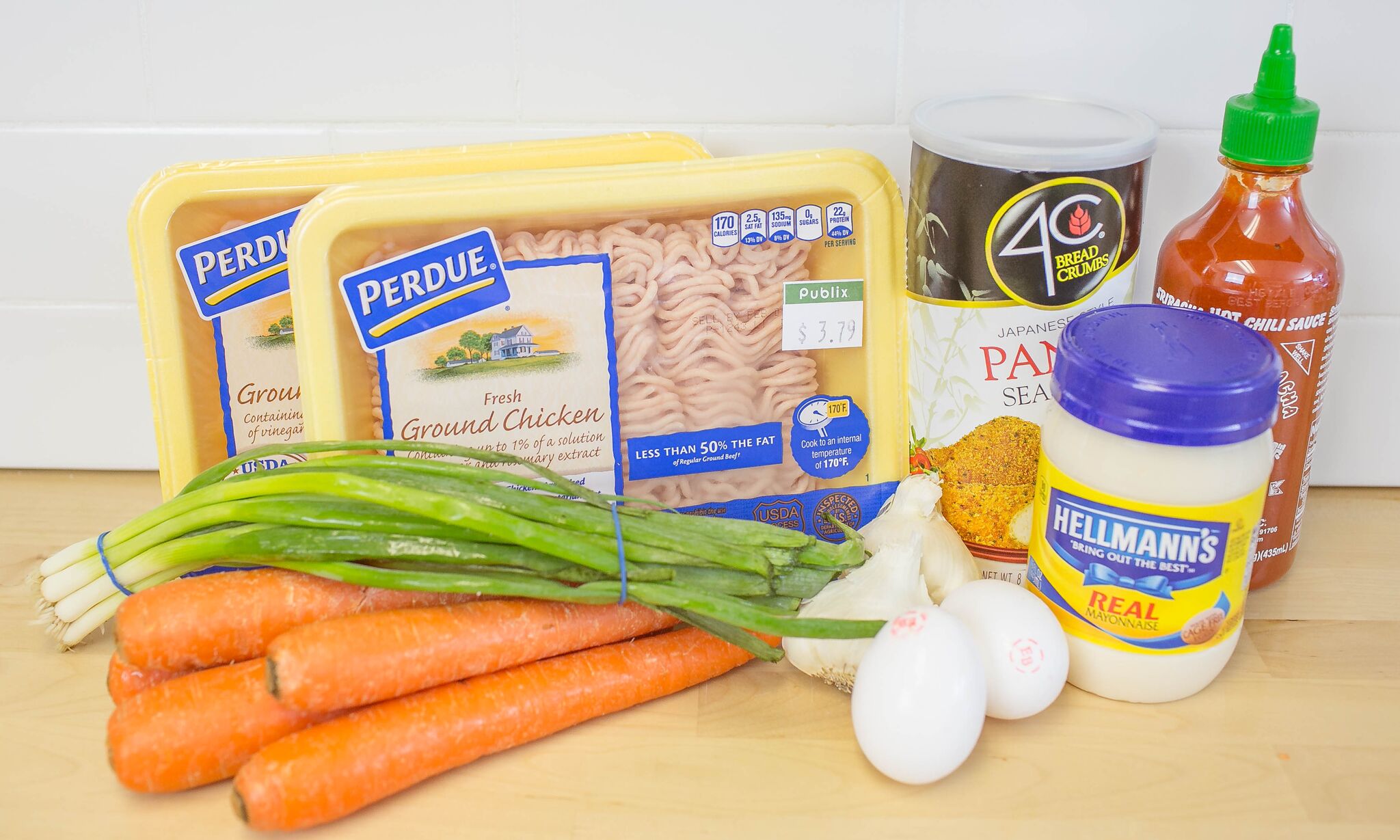 Assemble your ingredients for the chicken meatballs: ground chicken, green onion, carrots, eggs, garlic, mayonnaise, panko breadcrumbs, and sriracha hot sauce. 