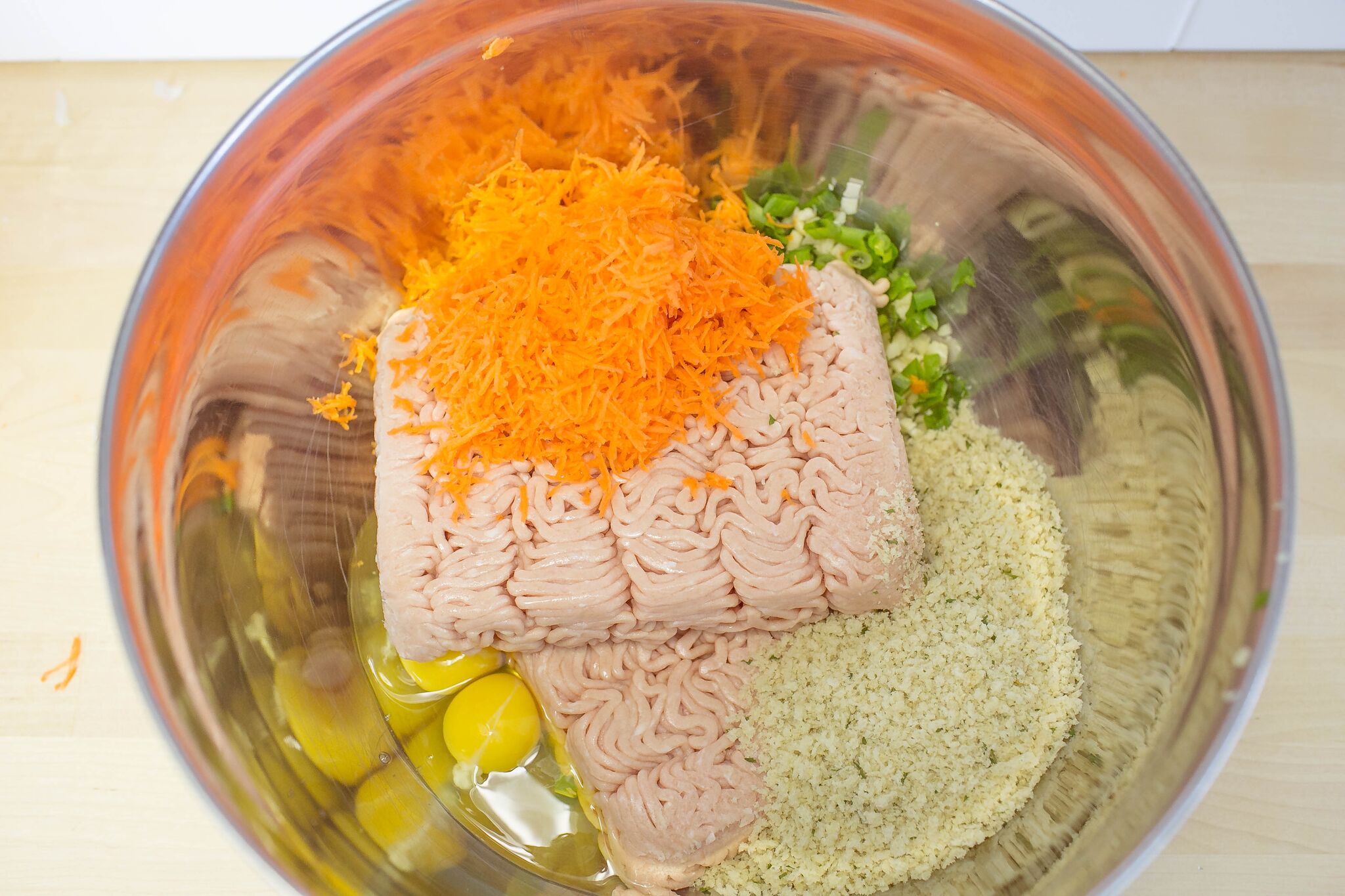 In a large bowl, mix together green onions, garlic, carrots, eggs, and panko into chopped meat.