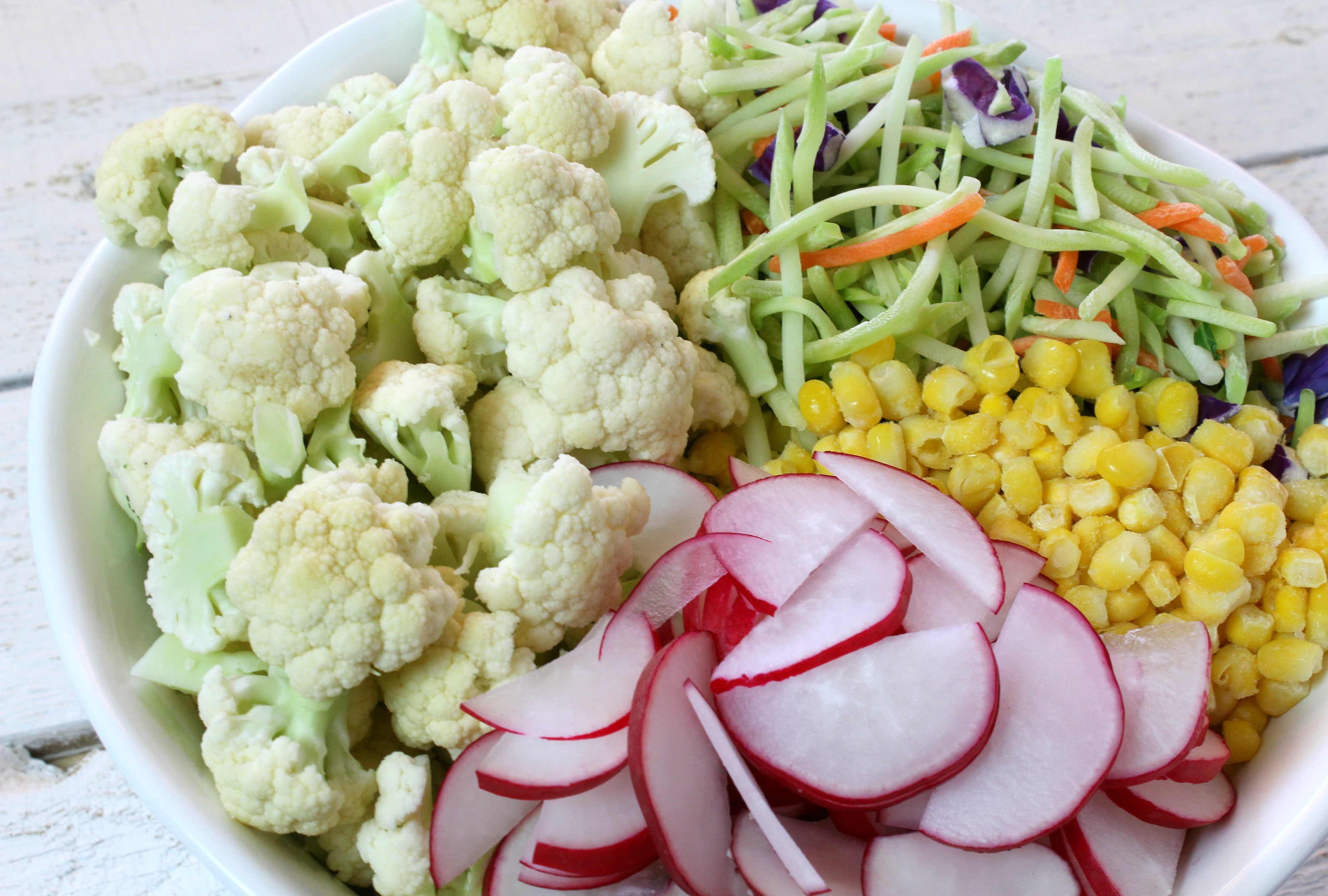 Place all broccoli slaw, cauliflower, corn, and radish in a large bowl.