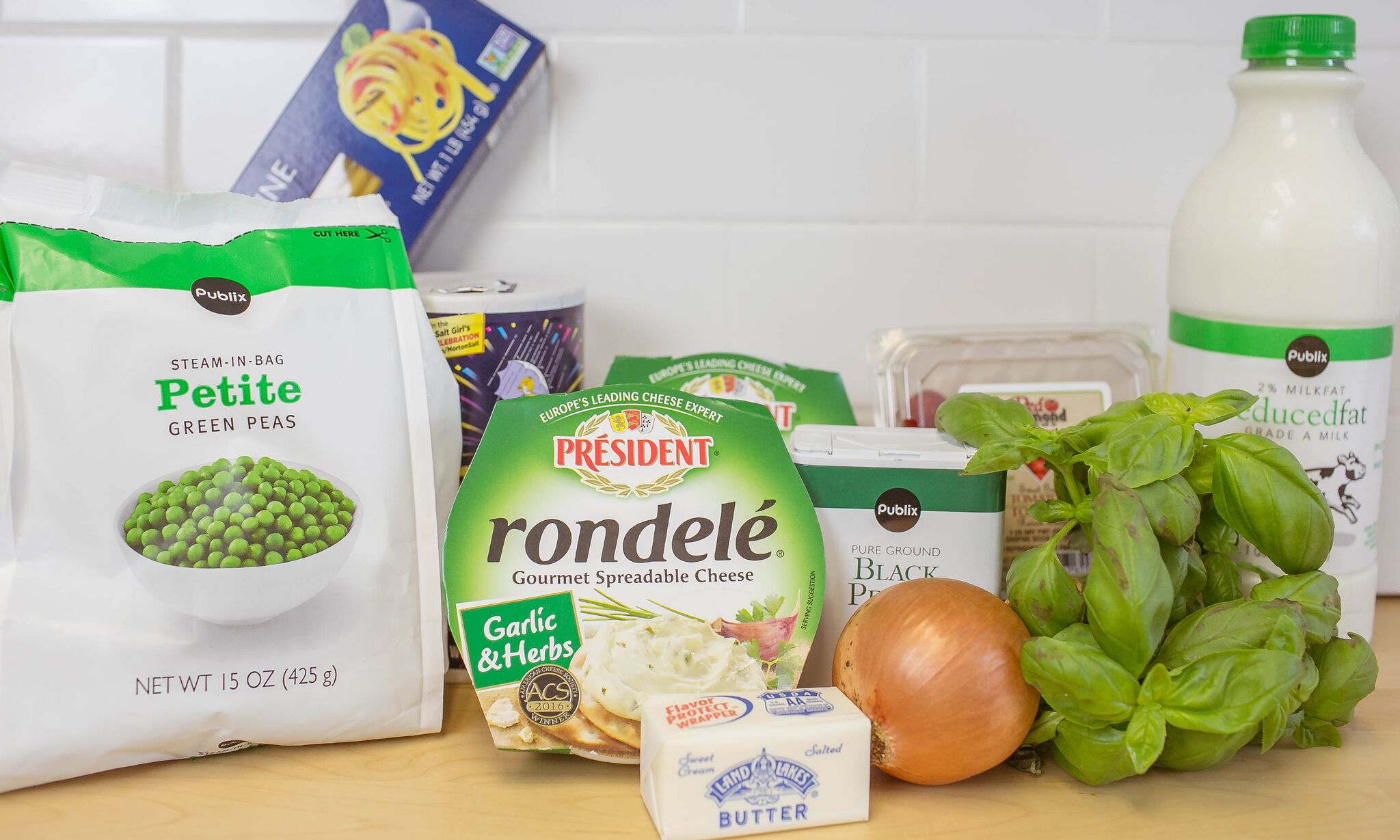 Assemble your ingredients for the pasta: basil, tomatoes, boxed pasta, milk, garlic and herb spreadable cheese, peas, onion, salt, pepper and butter. 