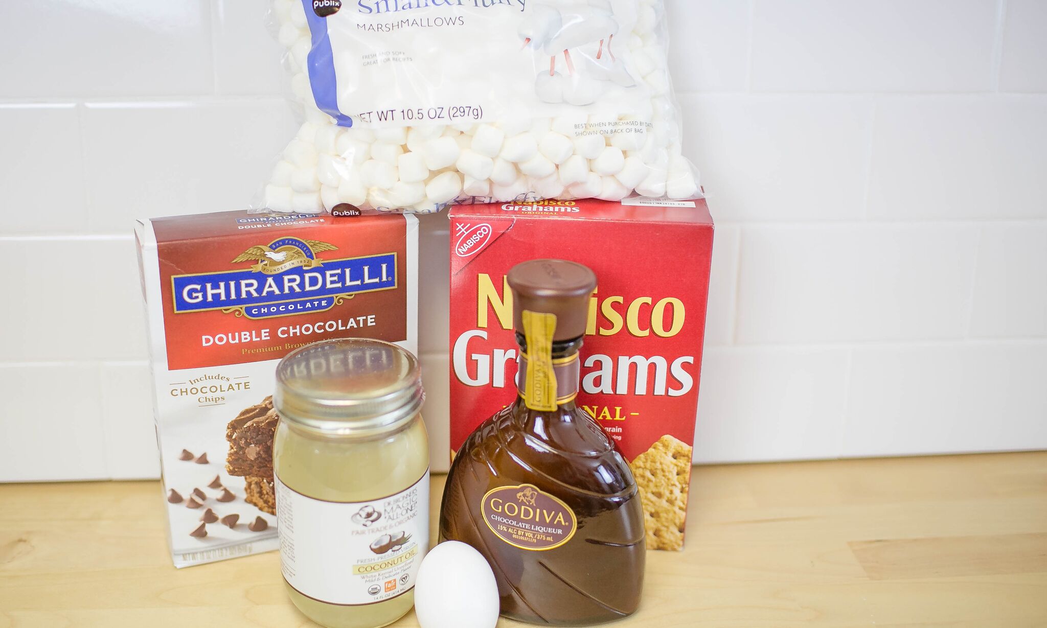 Assemble your ingredients for the brownie s'mores: brownie mix, one egg, Godiva liquor, coconut oil, mini marshmallows, and graham crackers. 