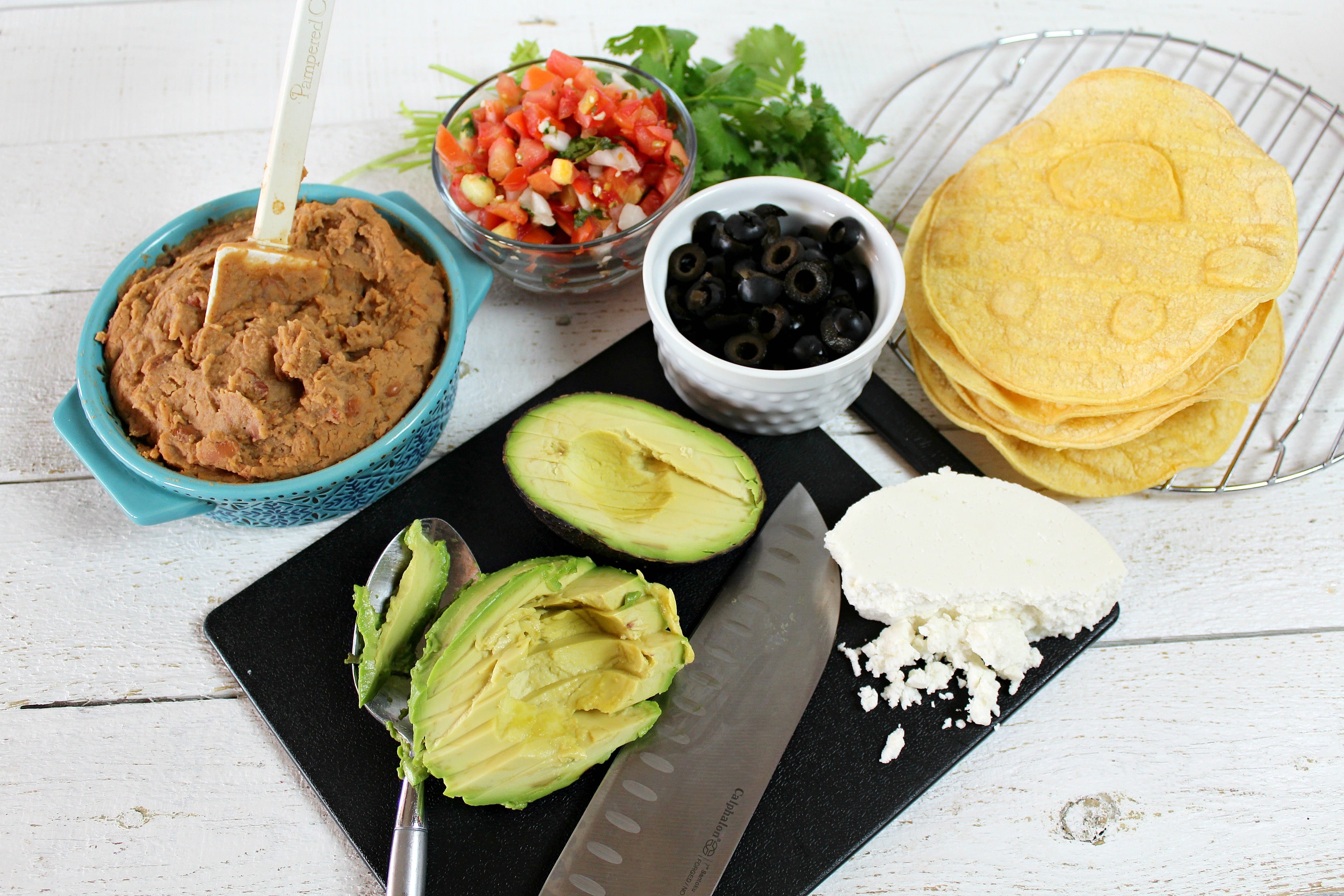 Slice the avocado and assemble the ingredients including the beans, salsa, cilantro, olives and of course, the tortillas. 