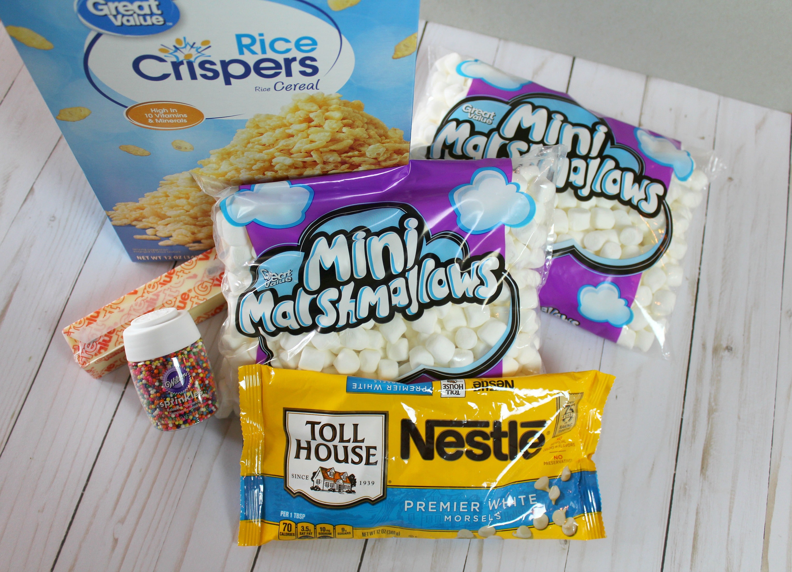 Assemble the ingredients for these yummy rice crispy treats: marshmallows, white chocolate chips, crispy rice cereal, sprinkles and butter. 