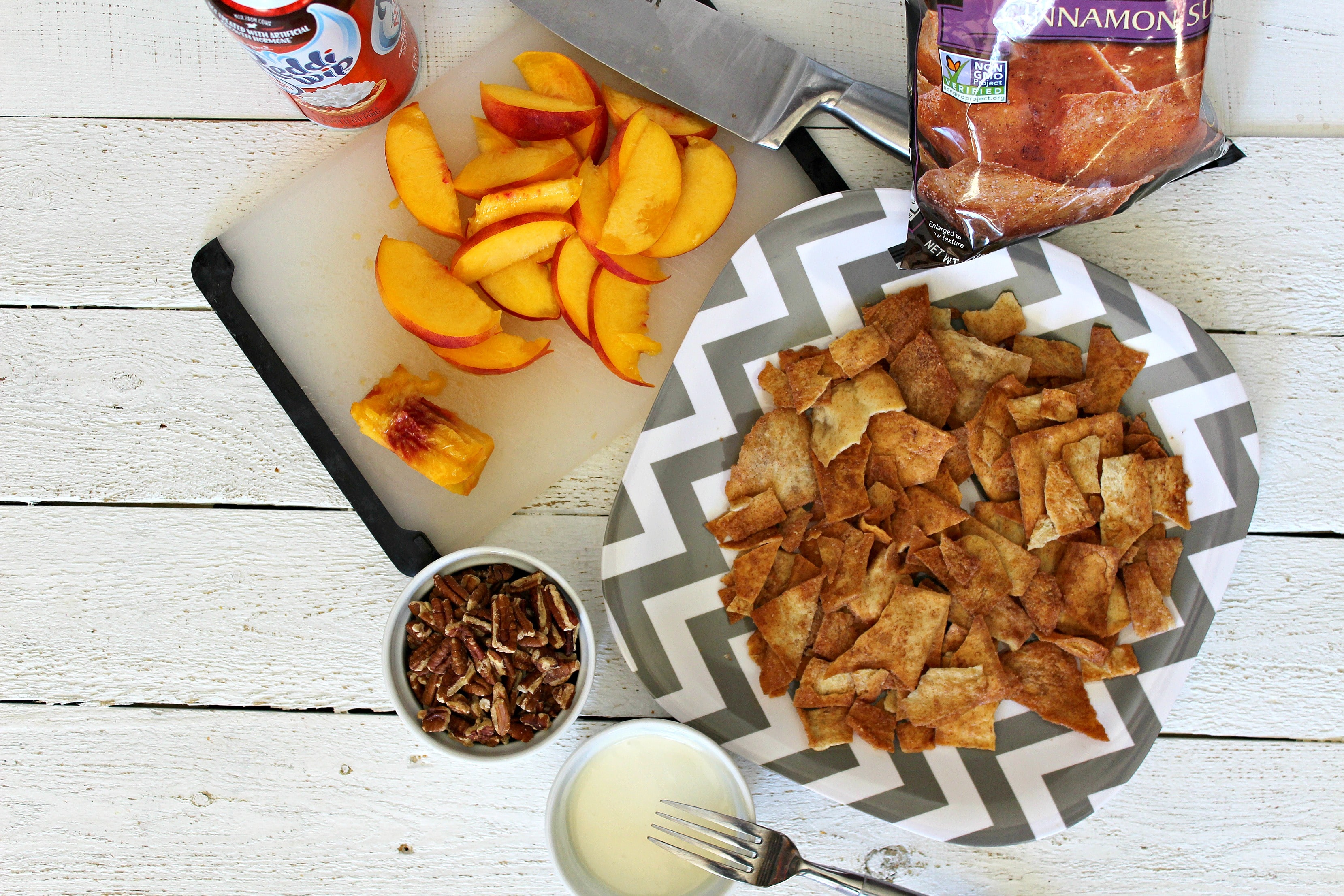 On a large plate layer cinnamon pita chips next to peaches and other ingredients. 