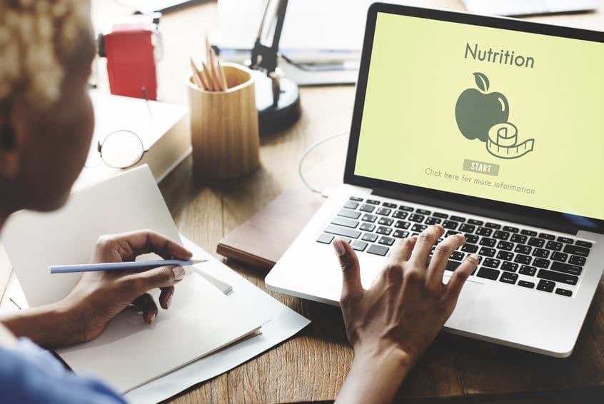 A woman tracking her eating on her laptop and in a notebook. 