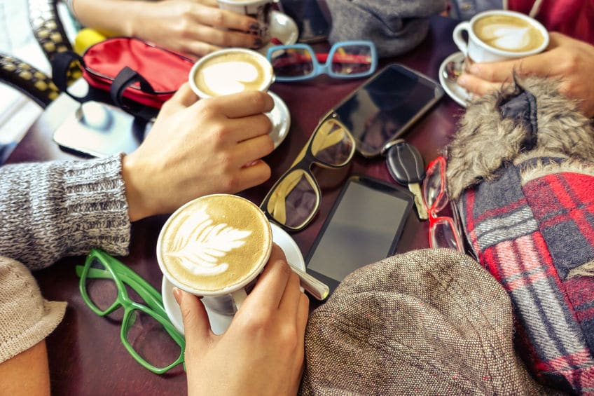 Friends enjoying beautifully made lattes with their phones, glasses and hats sitting on the table. 