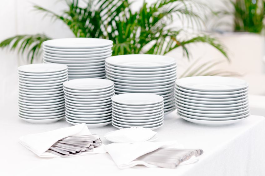 Clean white plates stacked and organized piles of utensils tucked in napkins. 