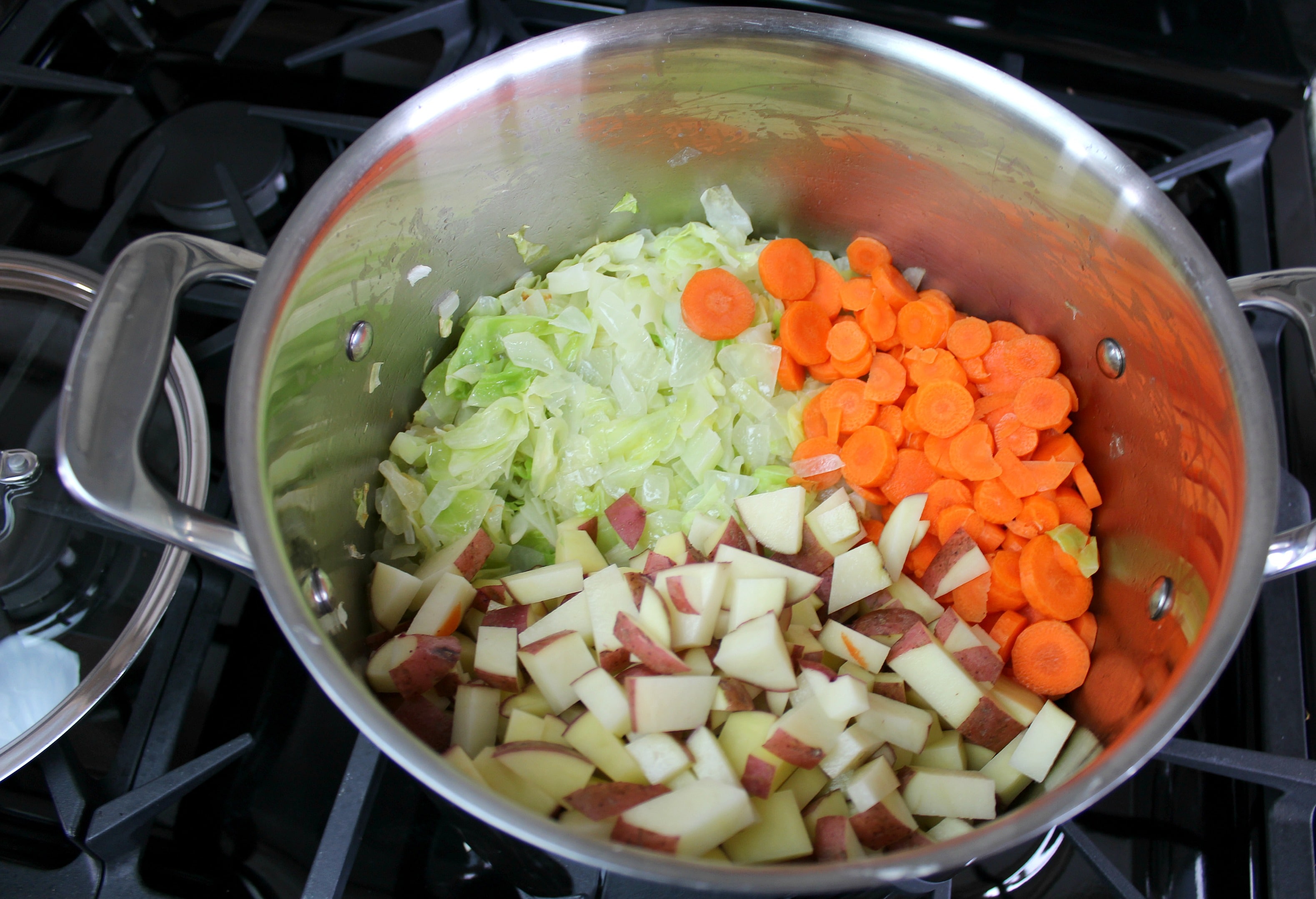 Add potatoes, carrots, and any other vegetables to the cabbage and onions.
