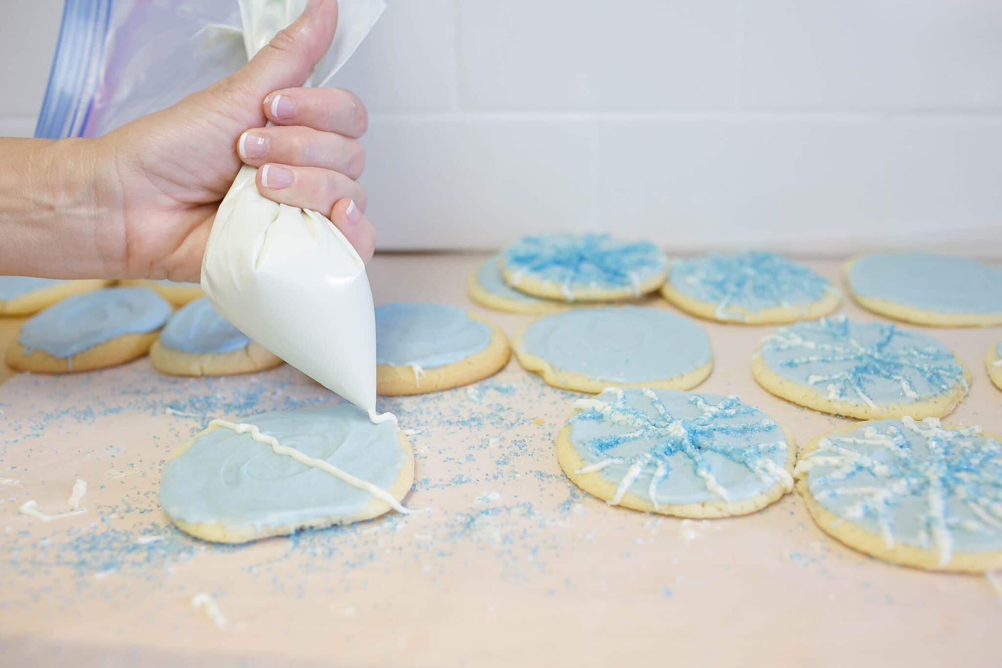 Pipe design on cookies using frosting and add colored sugars. 