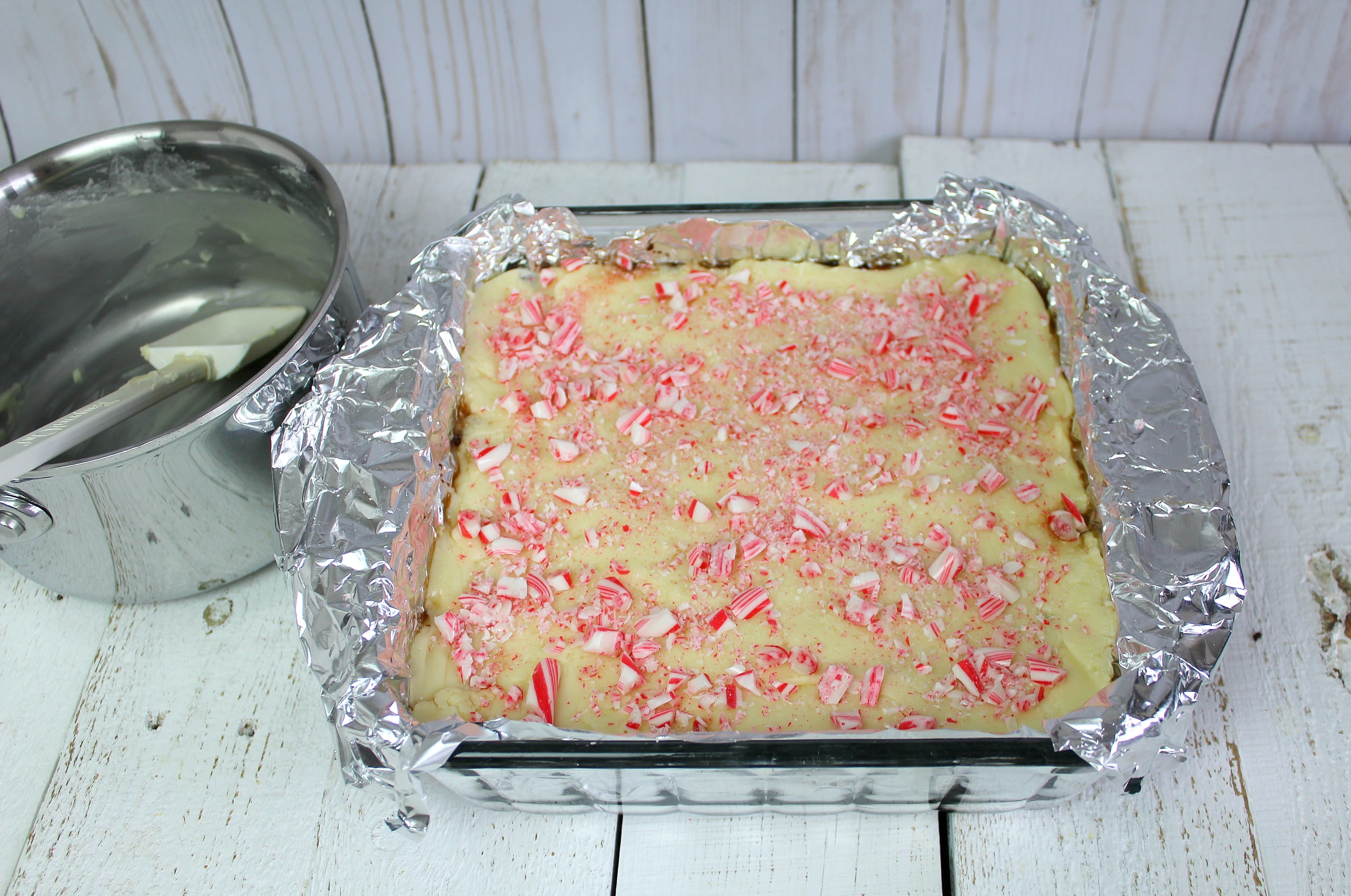 For the next step of the Easy Peppermint Bark Fudge recipe, spread the white chocolate on top of the dark chocolate and sprinkle with more yummy candy canes!