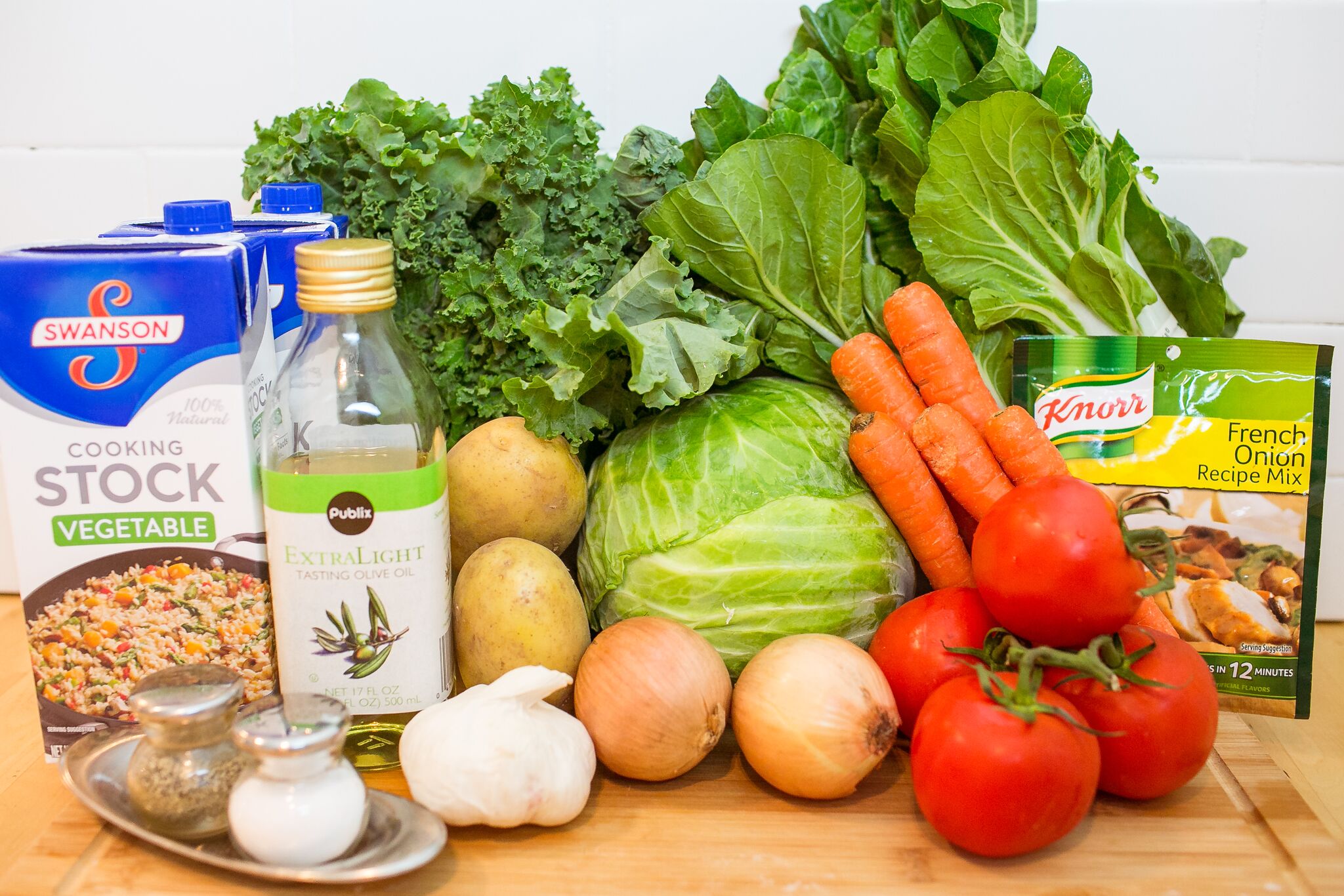 Assemble your ingredients for the winter diet soup: bok choy, kale, cabbage, olive oil, vegetable stock, tomatoes, yellow onions, garlic, salt, pepper, carrots, potatoes and french onion mix. 